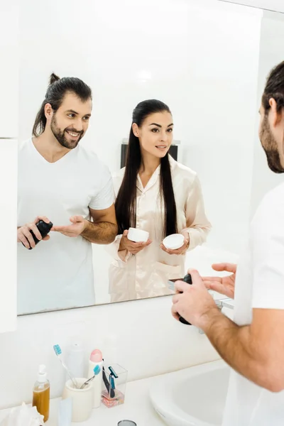 Привлекательная жена держит крем для тела, в то время как красивый муж наносит пену для бритья — стоковое фото