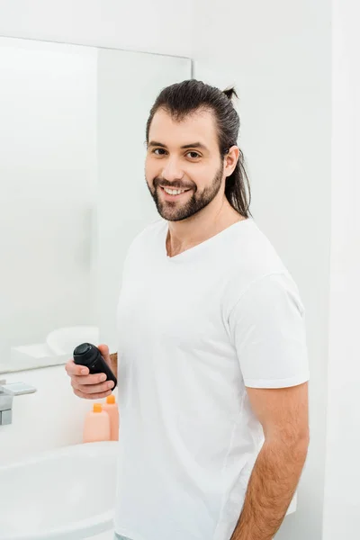 Hombre sosteniendo espuma de afeitar y sonriendo en el baño - foto de stock