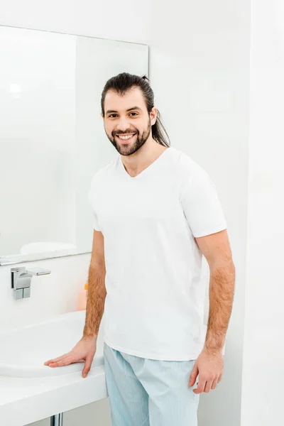 Hombre joven en camiseta blanca sonriendo en el baño - foto de stock