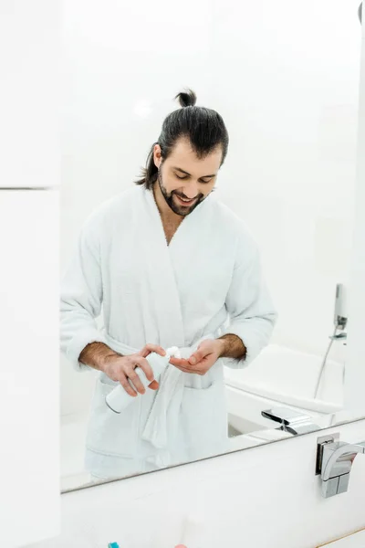 Handsome man holding shaving foam and smiling in front of mirror — Stock Photo