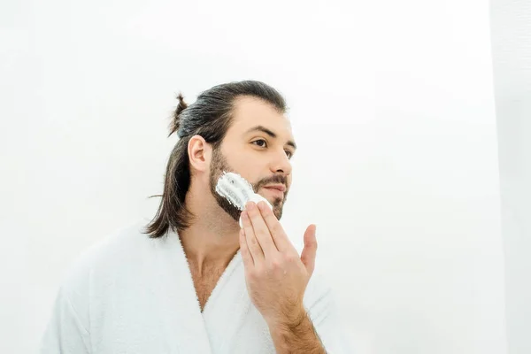 Homem adulto em roupão branco aplicando espuma de barbear — Fotografia de Stock