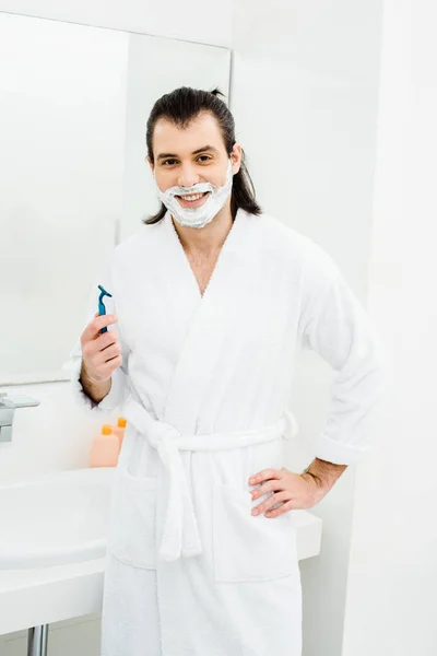 Красивый мужчина бреется и улыбается в ванной комнате — стоковое фото