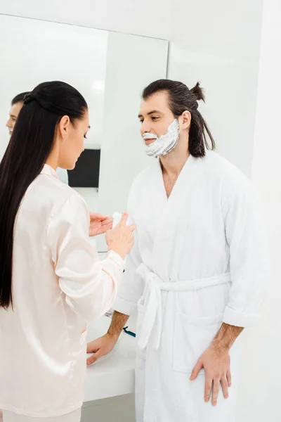 Mujer aplicando espuma de afeitar en la cara del marido - foto de stock