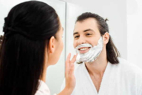 Mujer aplicando espuma de afeitar en la cara sonriente marido - foto de stock