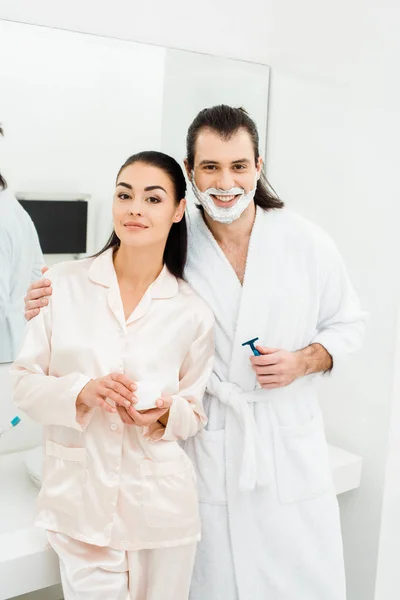 Linda pareja en batas blancas sonriendo en el baño - foto de stock