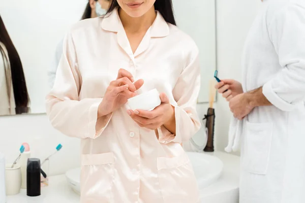 Обрезанный вид женщины с банкой крема для лица в ванной комнате — стоковое фото
