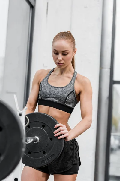 Attractive athletic sportswoman putting weights on barbell in gym — Stock Photo