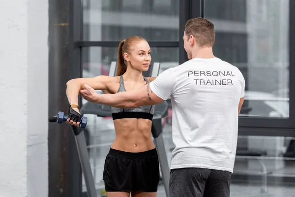 Entrenador personal ayudando a la deportista a hacer ejercicio con pesas en el gimnasio - foto de stock