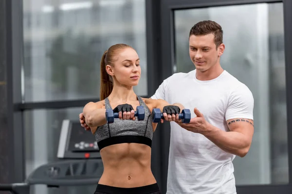 Bonito personal trainer ajudando desportista exercício com halteres no ginásio — Fotografia de Stock