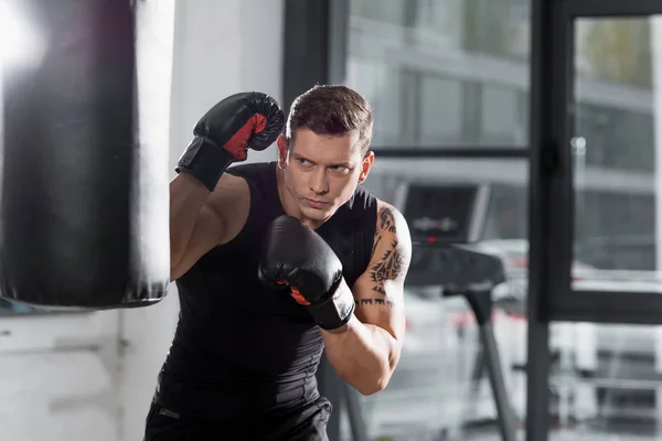 Tattooed muscular boxer exercising with punching bag in gym — Stock Photo