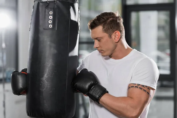 Boxer muscoloso tatuato che tiene il sacco da boxe in palestra — Foto stock