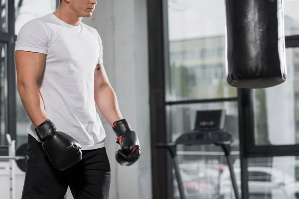 Abgeschnittenes Bild eines muskulösen Boxers, der in Turnhalle neben Boxsack steht — Stockfoto