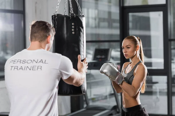 Trainer holding punching bag, attractive boxer training in gym — Stock Photo