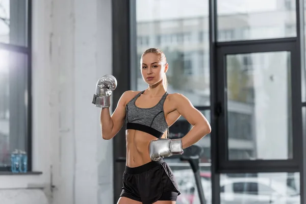 Fisiculturista muscular atraente posando com luvas de boxe de prata no ginásio e olhando para a câmera — Fotografia de Stock