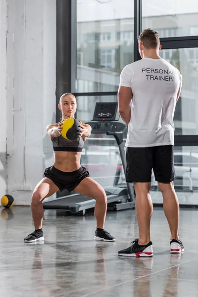 Vue arrière de l'entraîneur personnel regardant à l'entraînement sportif avec balle de remise en forme dans la salle de gym — Photo de stock