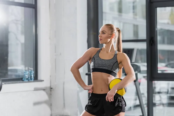Bodybuilder athlétique attrayant debout avec balle de fitness dans la salle de gym et regardant loin — Photo de stock
