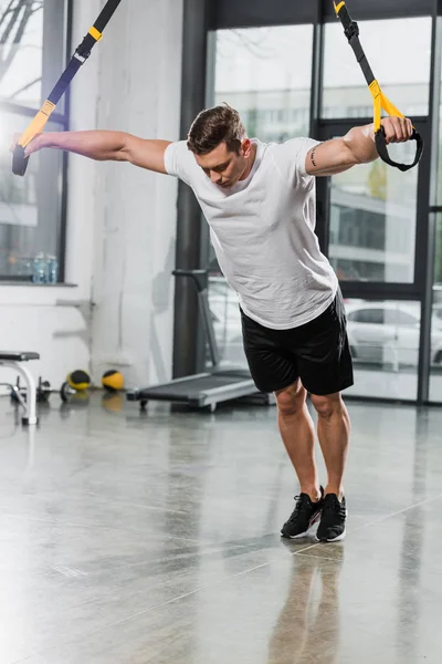 Fisiculturista muscular bonito trabalhando fora com tiras de suspensão no ginásio — Fotografia de Stock