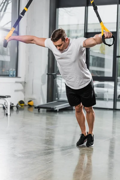 Handsome muscular bodybuilder working out with suspension straps in gym — Stock Photo