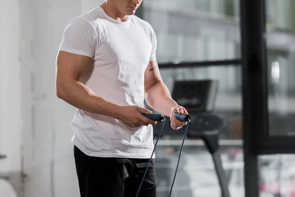 Image recadrée de bodybuilder athlétique debout avec corde sautante dans la salle de gym — Photo de stock