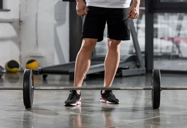 Immagine ritagliata di bodybuilder atletico in piedi vicino al bilanciere in palestra — Foto stock