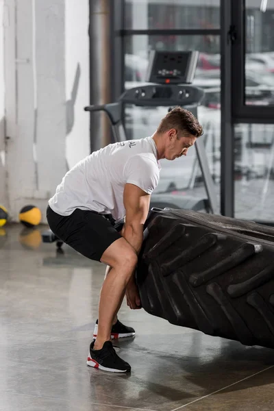 Vue latérale de bodybuilder musclé beau exercice avec pneu dans la salle de gym — Photo de stock