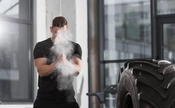 Guapo atlético culturista aplicando talco en polvo antes de entrenar con neumático en el gimnasio - foto de stock