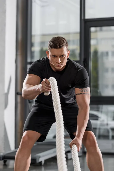 Schöner muskulöser Bodybuilder trainiert mit Seilen im Fitnessstudio — Stockfoto