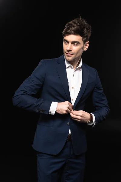 Handsome young businessman buttoning jacket and looking away isolated on black — Stock Photo