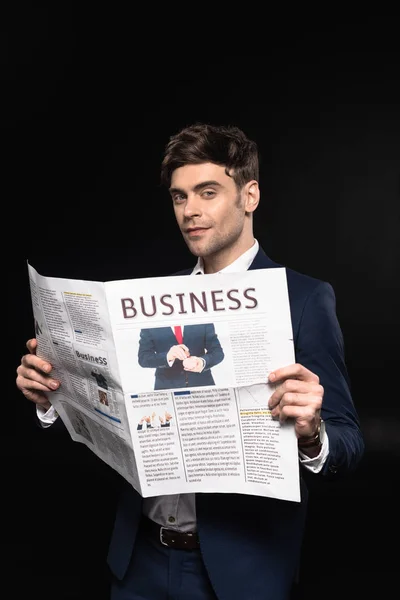 Attractive young businessman with newspaper looking at camera isolated on black — Stock Photo