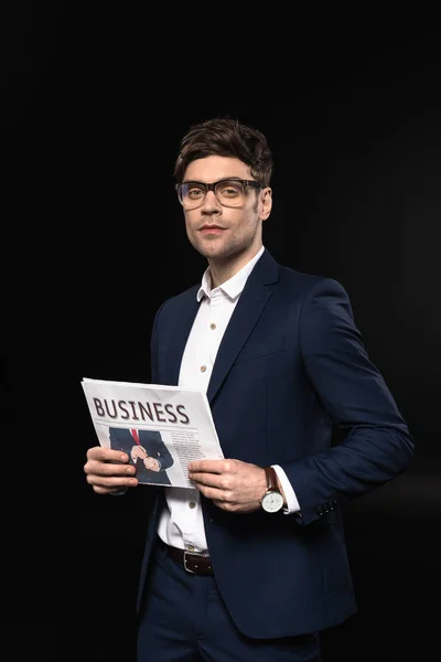 Schöner junger Geschäftsmann mit Zeitung, der auf schwarz isoliert in die Kamera blickt — Stockfoto
