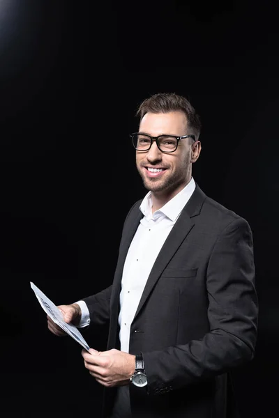 Souriant beau homme d'affaires avec journal regardant caméra isolée sur noir — Photo de stock