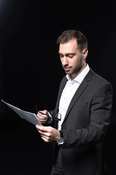 Attractive young businessman reading newspaper isolated on black — Stock Photo