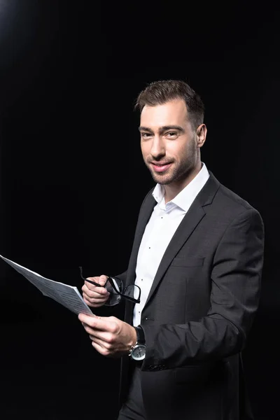 Happy young businessman with newspaper looking at camera isolated on black — Stock Photo