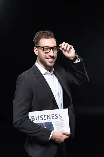 Handsome young businessman with newspaper looking at camera isolated on black — Stock Photo