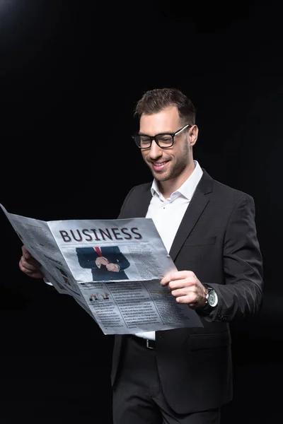 Handsome young businessman reading newspaper isolated on black — Stock Photo