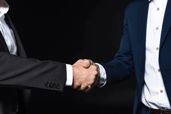 Tiro cortado de empresários apertando as mãos isoladas no preto — Fotografia de Stock