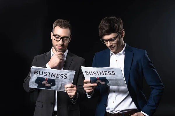 Selbstbewusste junge Geschäftsleute lesen Zeitungen isoliert auf schwarz — Stockfoto