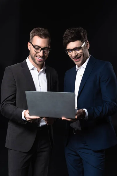 Happy young businessmen working with laptop together isolated on black — Stock Photo