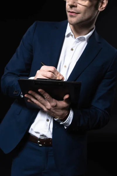 Cropped shot of young businessman writing in clipboard isolated on black — Stock Photo