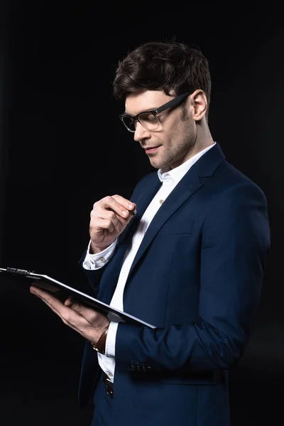 Handsome young businessman with clipboard isolated on black — Stock Photo