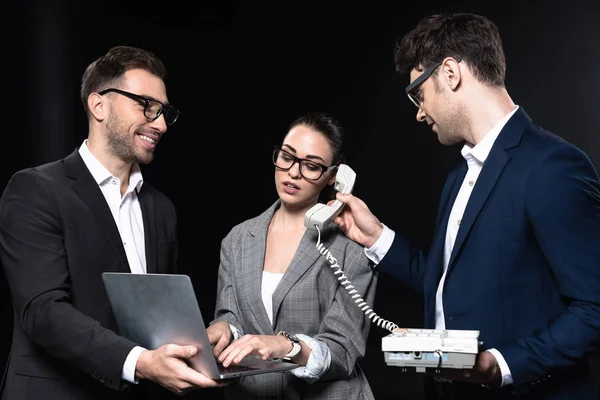 Overworked businesswoman talking by phone and working with laptop while colleagues supporting her isolated on black — Stock Photo