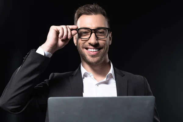 Happy young businessman with laptop looking at camera isolated on black — Stock Photo