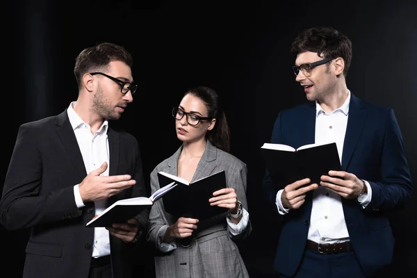 Grupo de empresarios serios que trabajan con cuadernos juntos aislados en negro - foto de stock