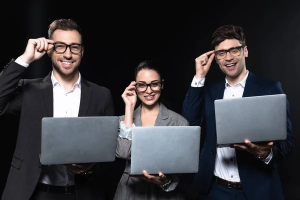 Group of smiling business people working with laptops together isolated on black — Stock Photo