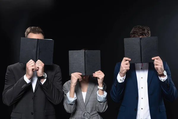 Group of business people covering faces with notebooks isolated on black — Stock Photo