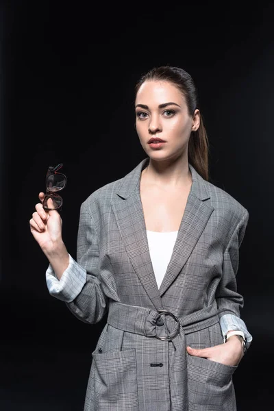 Attractive young businesswoman in plaid jacket with eyeglasses looking at camera isolated on black — Stock Photo