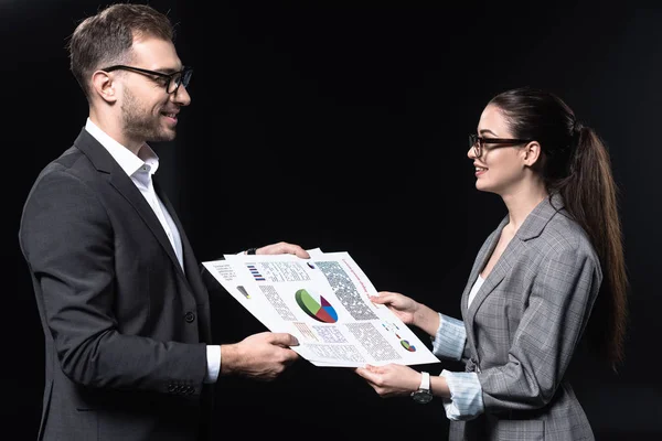 Jóvenes empresarios felices que pasan documentos con gráficos aislados en negro - foto de stock