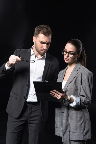 Serious business people with clipboard having conversation isolated on black — Stock Photo
