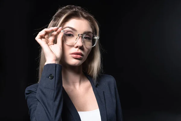 Atractiva joven mujer de negocios en traje elegante y gafas aisladas en negro - foto de stock