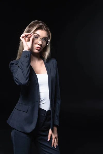 Hermosa joven mujer de negocios en traje elegante y gafas aisladas en negro - foto de stock